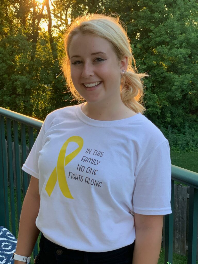 young woman wearing :In This Family No One Fights Alone" white t-shirt with yellow cancer awareness ribbon