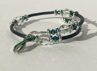 bracelet that crosses itself with big sparkle beads and a dark green cancer charm on one end