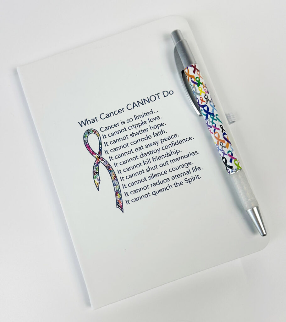 Image Shows our What Cancer Cannot Do® Journal which is a white journal, with our multicolored cancer awareness ribbon, and What Cancer Cannot Do® Peom printed on the front of the journal. The Journal includes a multicolored cancer ribbon pen with it and that is pictured as well.
