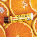 Picture of 1 stick of the Naked Bee USDA Organic Lip Balm in Orange Blossom Honey flavor displayed on a bed of oranges.