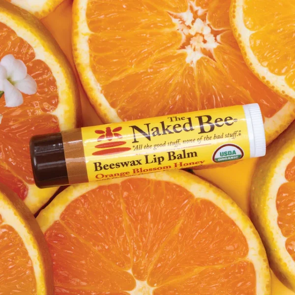Picture of 1 stick of the Naked Bee USDA Organic Lip Balm in Orange Blossom Honey flavor displayed on a bed of oranges.