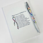 image showing the what cancer cannot do multicolored ribbon journal with multicolored ribbon pen that is included with the Chemo Care Package Gift Set.
