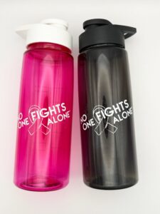Image showing our No One Fights Alone® Plastic Water Bottle in smoke and in hot pink colors, both with 'No One Fights Alone' and a cancer awareness ribbon printed on the water bottle in white ink.
