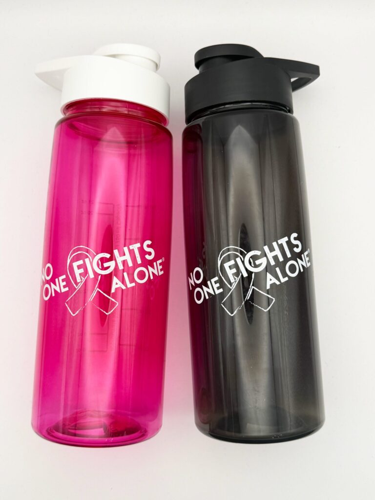 Image showing our No One Fights Alone® Plastic Water Bottle in smoke and in hot pink colors, both with 'No One Fights Alone' and a cancer awareness ribbon printed on the water bottle in white ink.